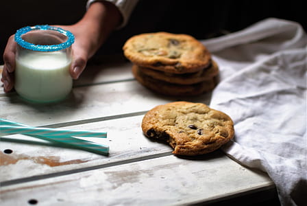 selective focus photography of person holding glass of milk beside cookie on tray thumbnail