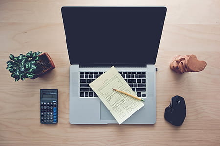 High Angle View of Home Office Desk Setup, with a MackBook, Calculator Indoor Desk Plant and a Wireless Mouse with Wooden Mini Statue. thumbnail