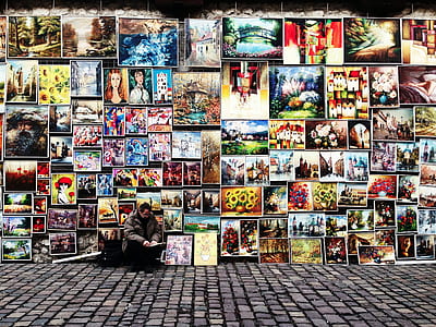man sitting in front of assorted paintings thumbnail