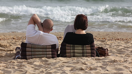 two man and woman lying on beach near water thumbnail