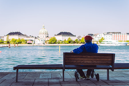 person in blue 3/4-sleeved shirt sitting on brown wooden bench near body of water during daytime thumbnail