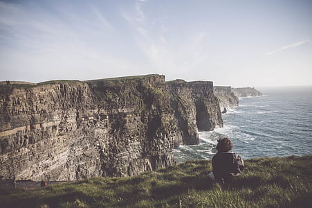 person sitting on cliff near ocean during daytime thumbnail