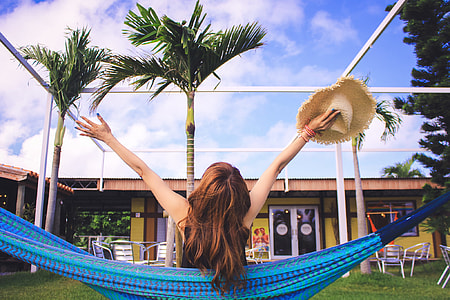 woman sitting on blue hammock white holding a brown straw hat thumbnail