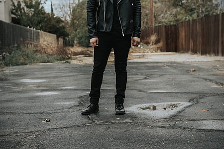 man wearing black jacket and pants standing between wooden fences thumbnail