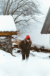 man in brown fur-trim hooded jacket wearing red knit cap walking on snow-terrain during daytime thumbnail