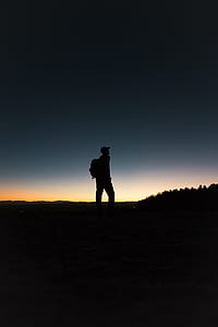 silhouette of person carrying backpack standing near trees at golden hour thumbnail