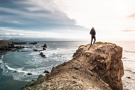 man standing on cliff in front of sea thumbnail