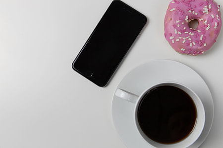 Coffee cup, iPhone mobile smartphone and donut on white desk thumbnail