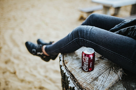 Beautiful blonde woman relaxing with a can of coke on a tree stump by the beach thumbnail