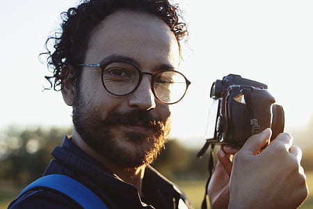 man wearing eyeglasses holding DSLR camera thumbnail