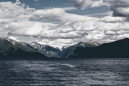 body of water near mountains under cloudy skies thumbnail
