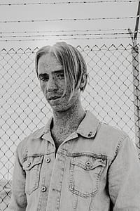 gray scale photo of a man behind cyclone fence thumbnail