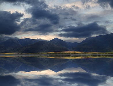 mountain range reflecting on the ocean under cloudy sky thumbnail