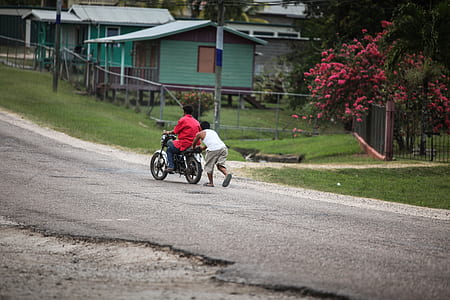 man pushing motorcycle with man riding during daytime thumbnail