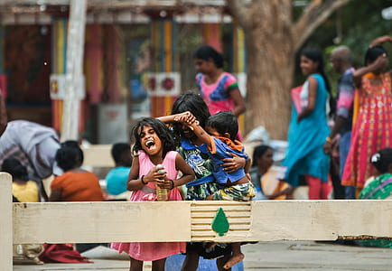 selective focus of three children laughing near wooden fence during daytime thumbnail