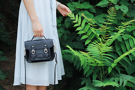 Woman Holding Black Leather Bag And Standing Beside Green Plant thumbnail