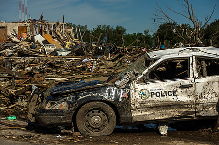 broken police car surrounded  by wither tree and house thumbnail