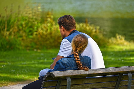 man wearing white polo shirt sitting beside woman wearing denim jacket both sitting on wooden bench thumbnail