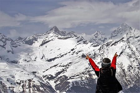 man standing in front of mountains covered by snow while pointing at it thumbnail