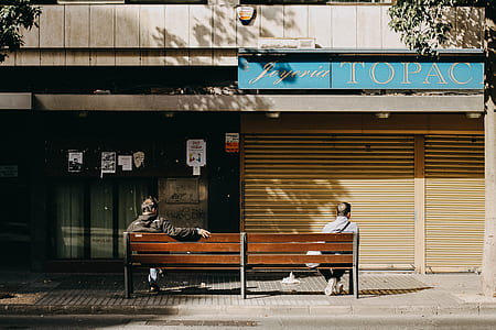 two men sitting on brown bench facing store thumbnail
