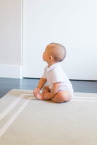 baby boy sitting on brown area rug looking up thumbnail