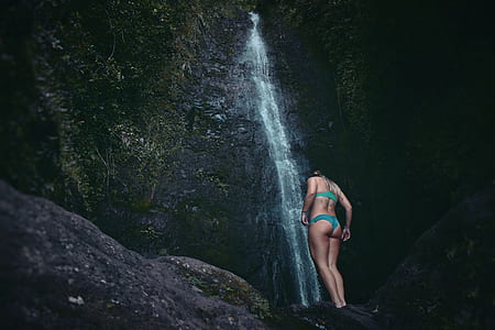woman in teal bikini standing on rocks near waterfall thumbnail