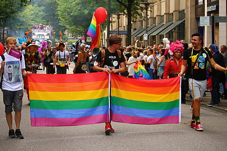 three men walking on road holding LGBT flag during daytime thumbnail