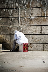 person sitting on red plastic crate beside concrete wall thumbnail