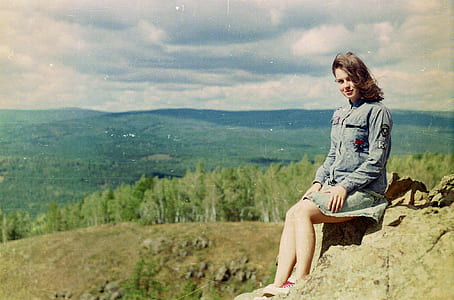 woman sitting on rock ledge near tall trees thumbnail