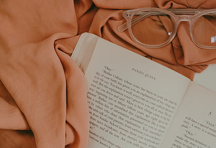 opened Daniel Quinn book near brown textile and brown framed wayfarer-style eyeglasses thumbnail