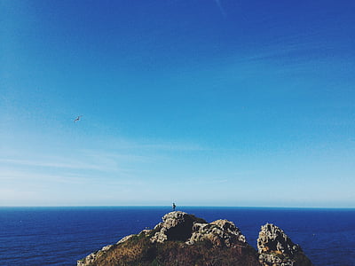 person standing on gray peak front of sea at daytime thumbnail