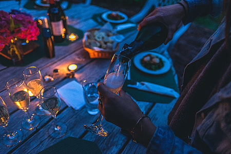 person pouring champagne on champagne flute while standing on brown wooden table with food on top thumbnail