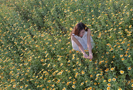 woman wearing white dress standing on daisy flowers field during daytime thumbnail