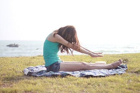 woman sitting on blue textile while stretching during daytime thumbnail