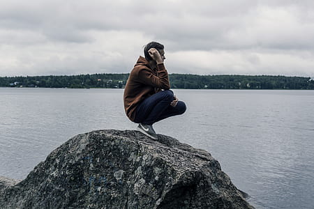 man sitting on rock near body of water thumbnail
