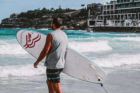 Man Walking Towards Body Of Water Holding A Surfboard thumbnail