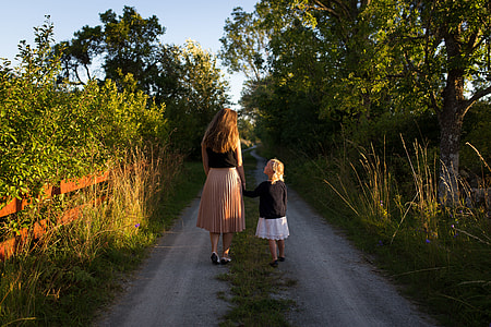 woman and girl walking on the street with many trees during daytime thumbnail