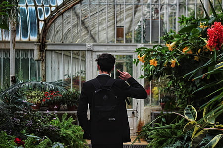 man showing middle finger standing near flowers and green house thumbnail