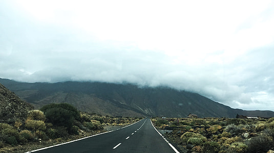 empty road leading to mountain covered in cumulus clouds thumbnail