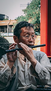 man playing flute beside stone thumbnail