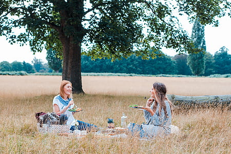 two women sitting on mat under tree thumbnail