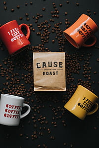 four assorted-color ceramic mugs on black surface with coffee beans thumbnail