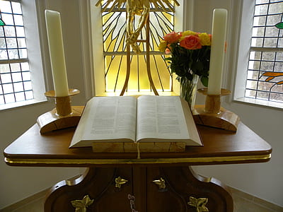 open bible between two white pillar candles on table thumbnail