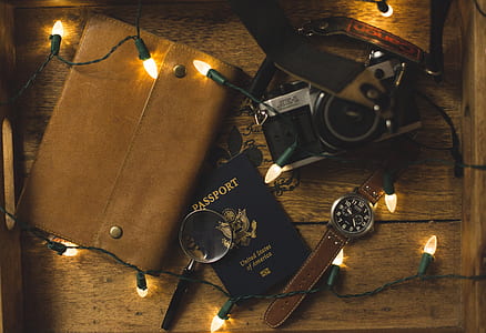 round black chronograph watch beside black wooden handled magnifying glass, Passport, and DSLR camera thumbnail