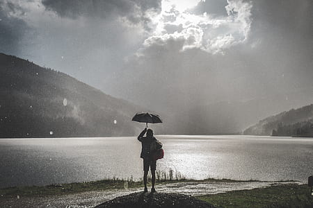 person holding umbrella standing beside body of water thumbnail