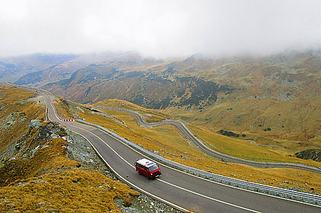red van cruising uphill road under cloudy sky during daytime thumbnail