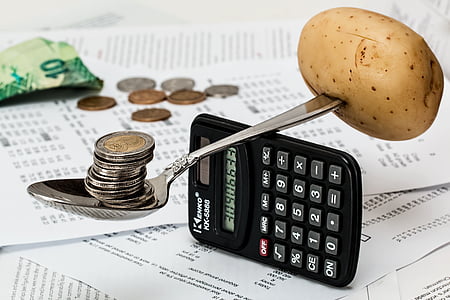 brown potato and round silver-and-gold-colored coins stack balancing on gray steel spoon and black digital calculator thumbnail