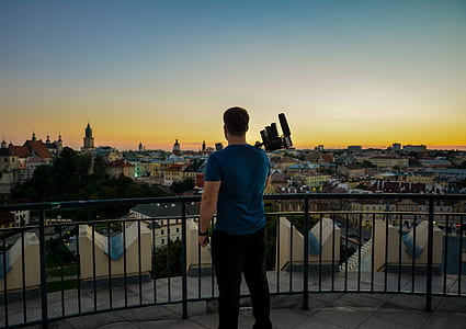 man wearing blue t-shirt standing on roof-top in front of houses and buildings thumbnail