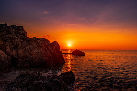 rock boulder and cliff beside body of water under sunset sky thumbnail