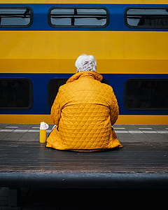 person in yellow top sitting on bench in front of train thumbnail
